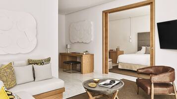 A modern hotel room with a sofa, a desk, a chair, a bed, and a TV.
