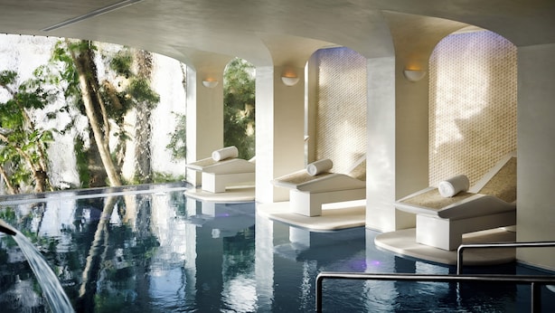Una piscina interna moderna con acqua cristallina, circondata da lettini prendisole e vista sugli alberi.