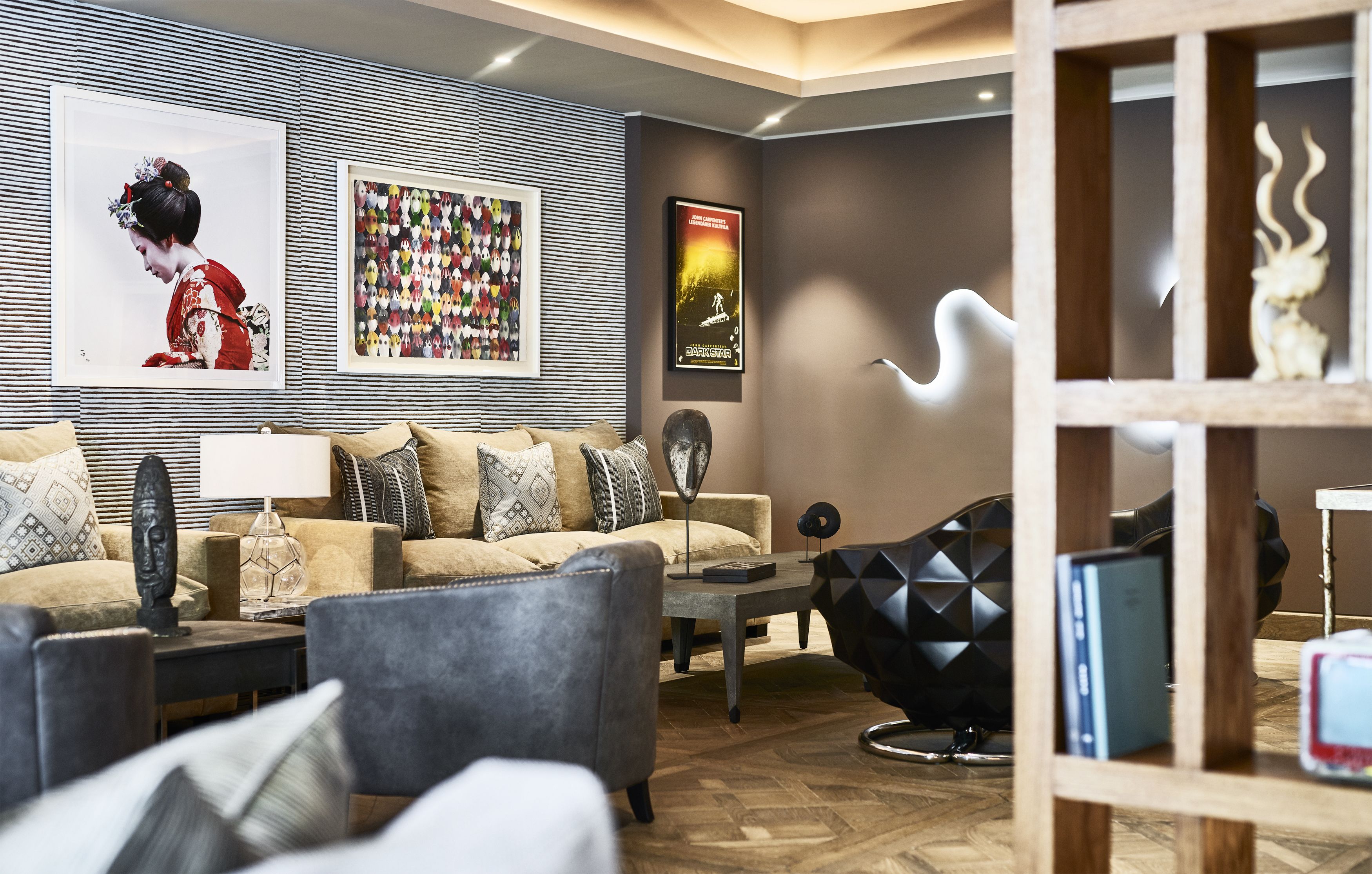 A modern living room with a sofa, armchairs, a coffee table, and a TV stand. There are framed pictures on the wall and a decorative sculpture on the coffee table.