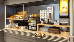 A breakfast bar with a coffee machine, a refrigerator with beverages, and a display of fruits.