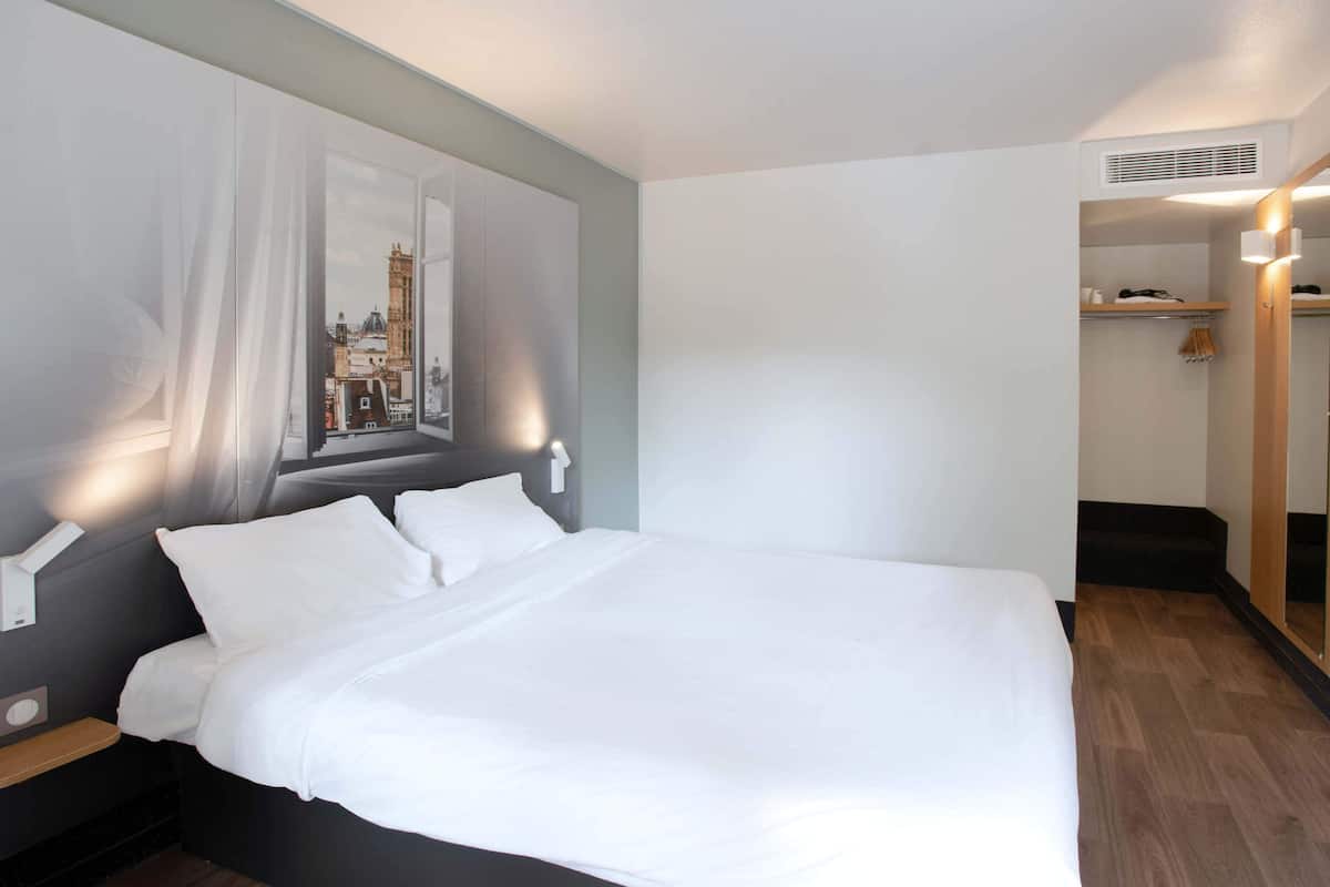 Habitación de hotel moderna con una cama grande, un cuadro de paisaje urbano en la pared, suelo de madera y un pequeño rincón con asientos.