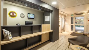 A hotel reception area with a reception desk, a digital screen, a calendar, and a seating area with a table and chairs.