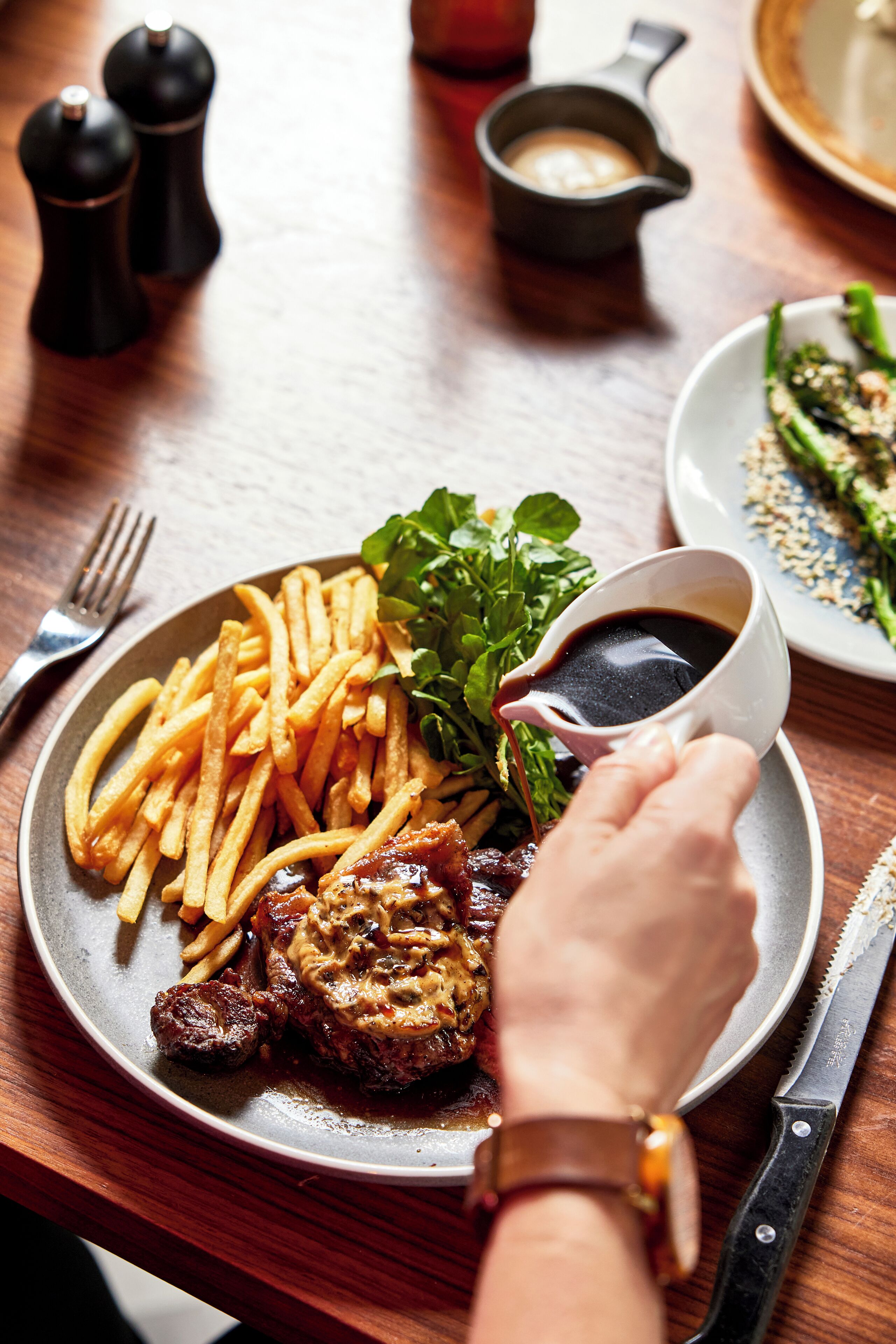 En tallerken med mad, pommes frites, steak og sauce, der hældes på.