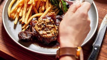 En tallerken med mad, pommes frites, steak og sauce, der hældes på.