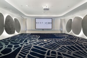A large conference room with a dark patterned carpet, a large screen displaying 'WEST CURIO HOTEL' branding, and a projector mounted on the ceiling. - West Hotel Sydney, Curio Collection by Hilton (Sydney)