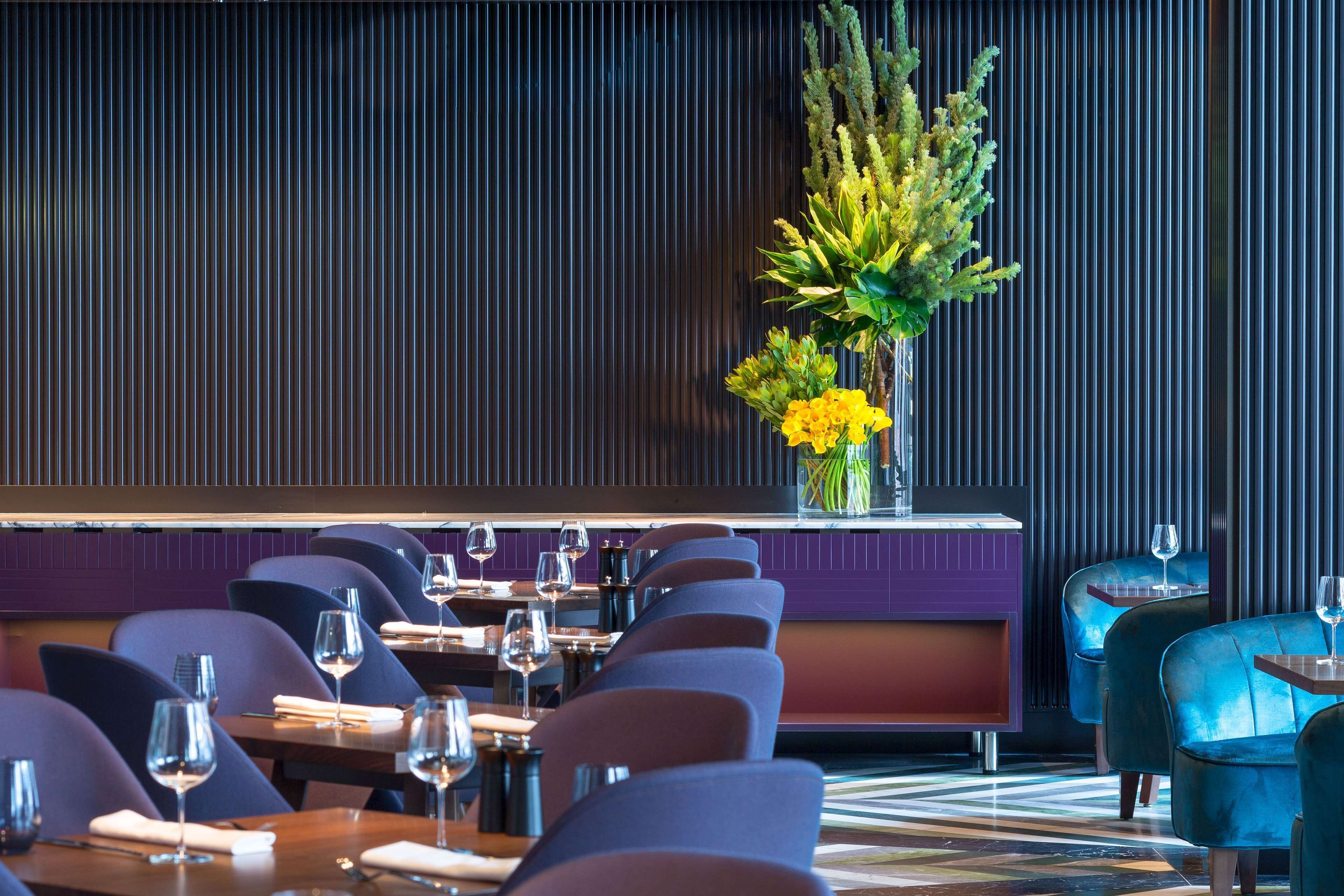 A restaurant with a modern interior, featuring a long table with chairs, a decorative plant, and a purple wall.