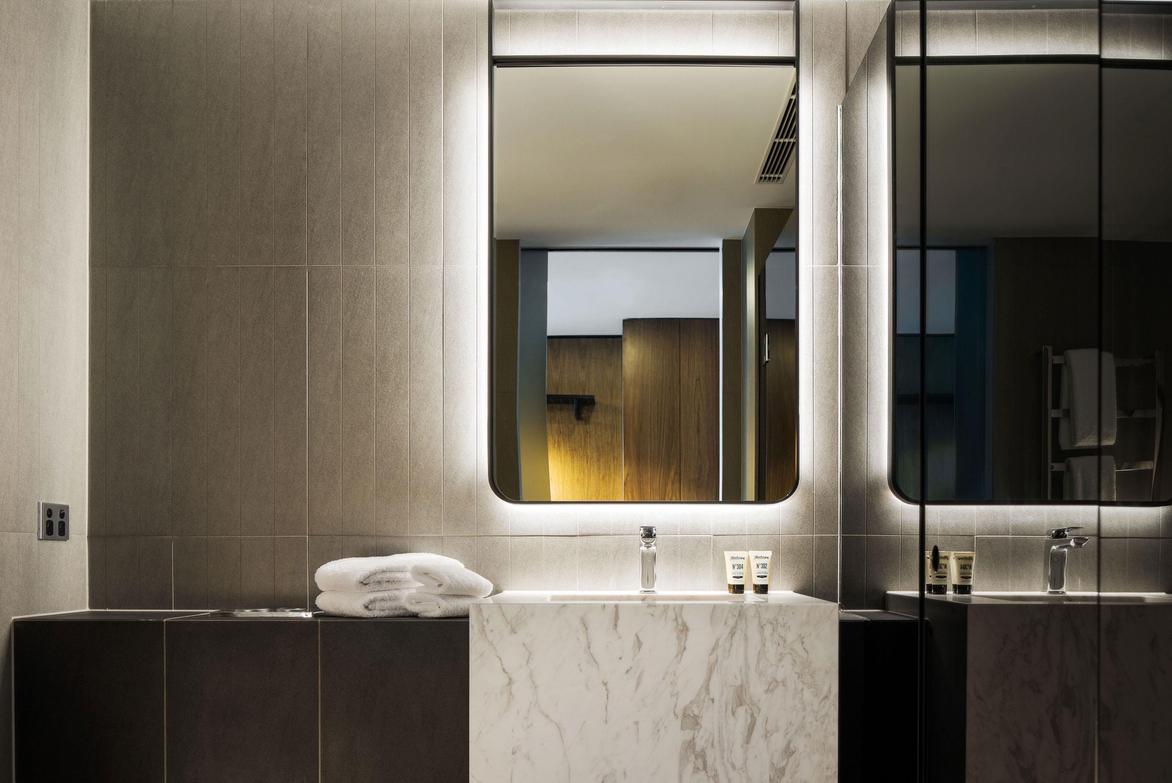 A modern bathroom with a marble sink, a towel on the counter, and a mirror reflecting the room.