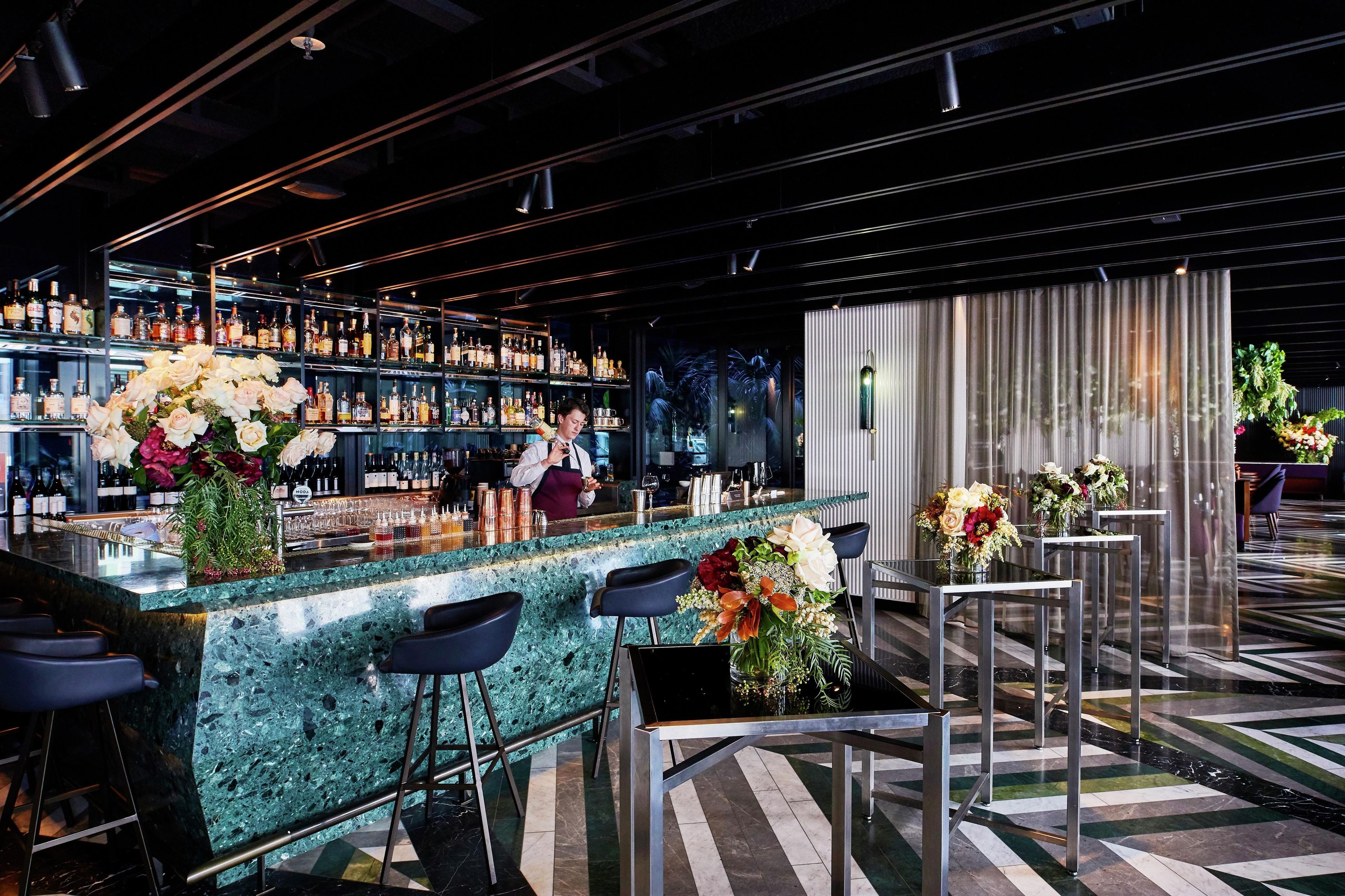 A bar area with a marble countertop, multiple bar stools, and a bartender.