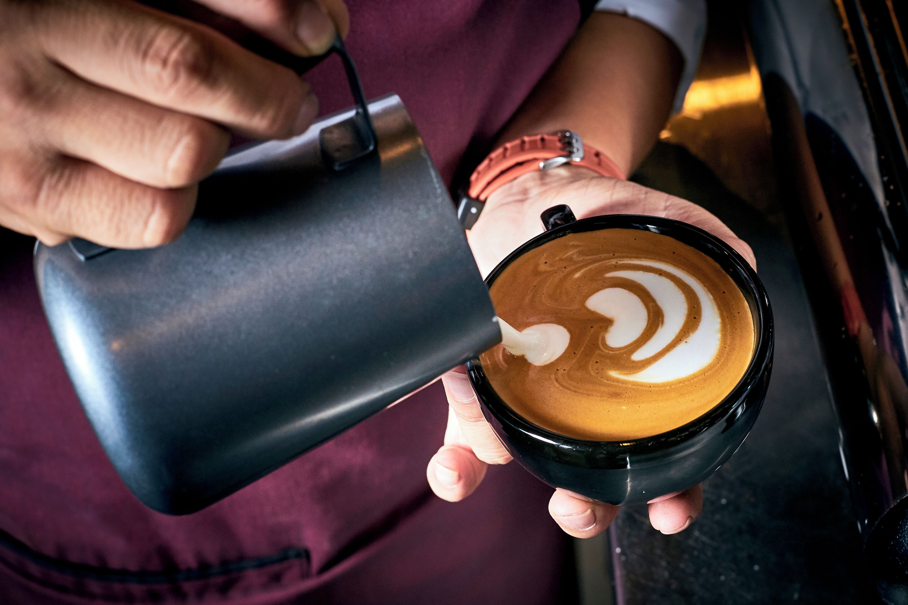 A person holding a cup of coffee with latte art.