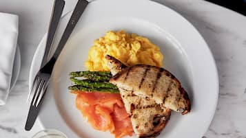 A plate with grilled chicken, asparagus, and salmon on a white plate, accompanied by a fork and knife, and a glass of white wine.