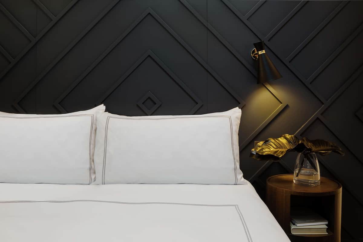 Un lit bien fait, avec du linge de lit blanc, et un mur sombre à motifs géométriques derrière.