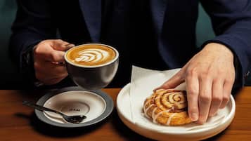 A person holding a cup of coffee with latte art, a plate with a croissant, and a spoon on a table.