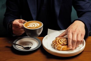 A person holding a cup of coffee with latte art, a plate with a croissant, and a spoon on a table. - West Hotel Sydney, Curio Collection by Hilton (Sydney)