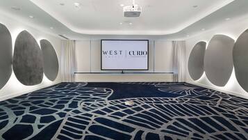 A conference room with a large screen displaying "WEST CURIO HOTEL" and a patterned carpet.