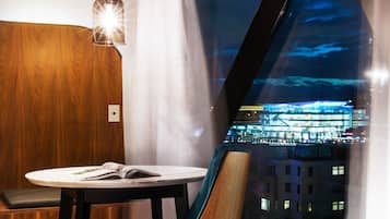 A modern room with a large window, a round table, a blue chair, and a hanging light fixture.