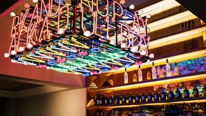 A bar with a neon sign spelling "NECKLACE" and shelves stocked with liquor bottles. - LUME Boutique Hotel, Autograph Collection (Frankfurt)