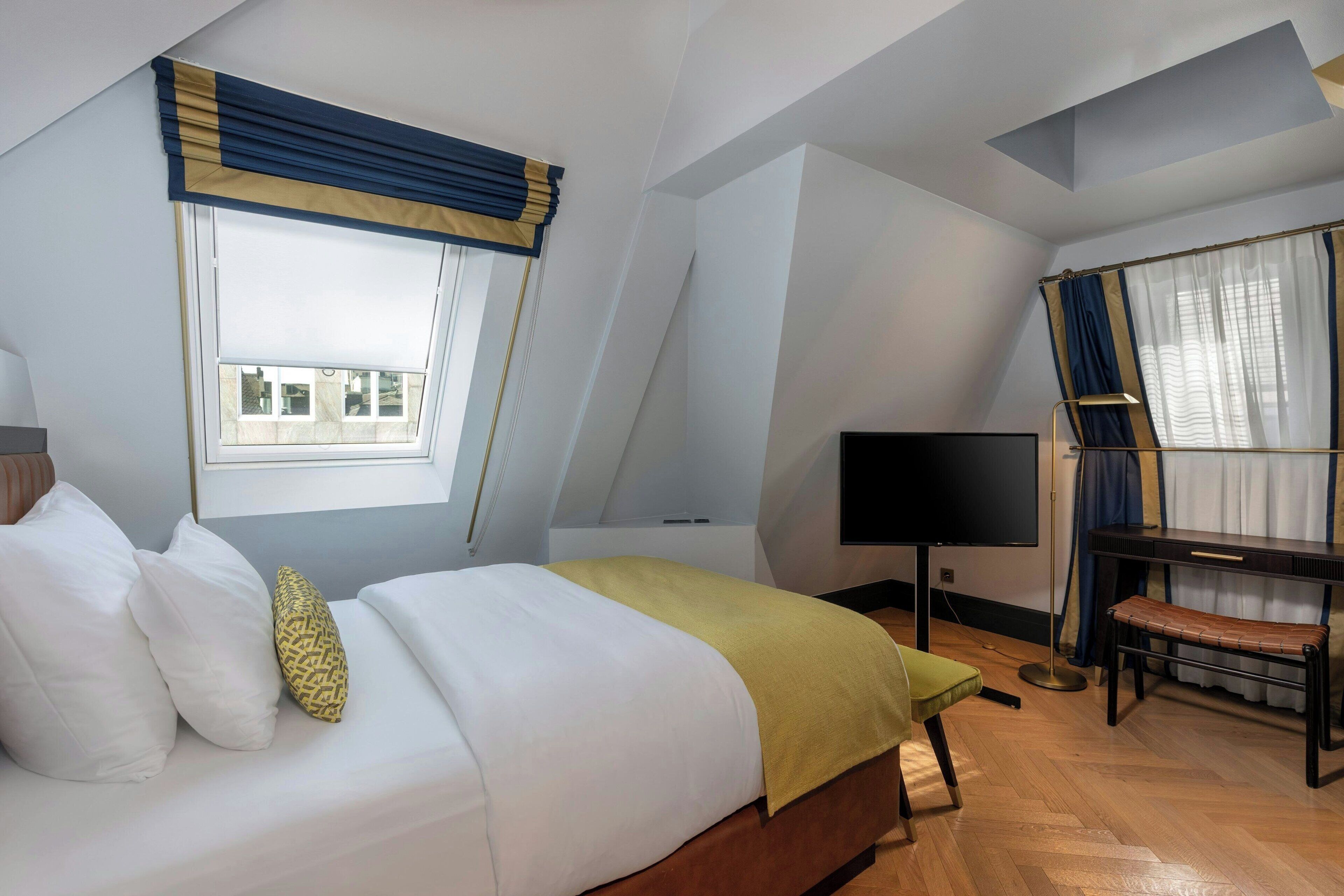 Un dormitorio con una cama, un escritorio, una silla, un televisor y una ventana con cortinas.
