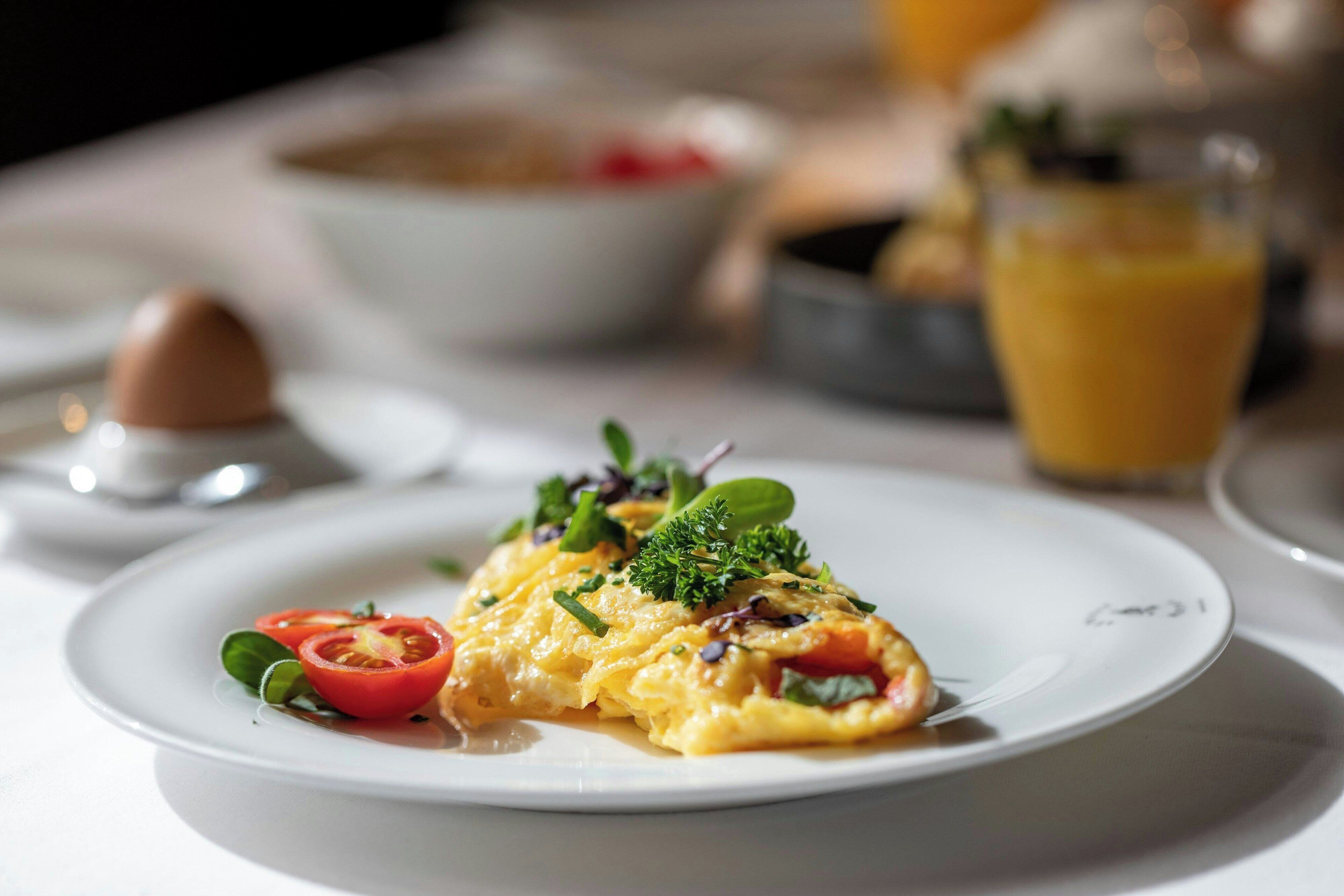 A plate of scrambled eggs with vegetables and herbs, a glass of orange juice, and a small bowl of red sauce on a table.