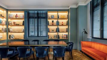 A dining area with a long wooden table, six blue chairs, and a red sofa. Shelves with books and decorative items line the walls.