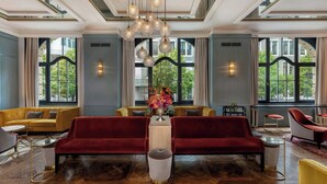 A spacious lobby with a red sofa, yellow sofa, and red armchairs, a large vase with flowers, and large windows with a view of greenery. - LUME Boutique Hotel, Autograph Collection (Frankfurt)