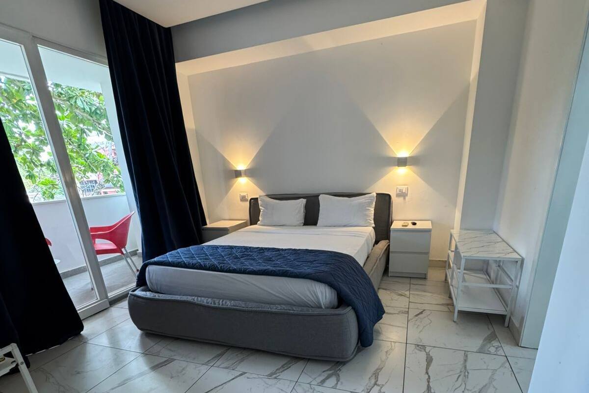 A modern bedroom with a bed, nightstands, and a marble-tiled floor.