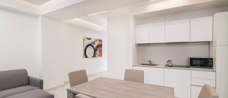 Une pièce moderne et minimaliste comprenant une table à manger, des chaises, un canapé et un coin cuisine avec des placards et des appareils électroménagers.