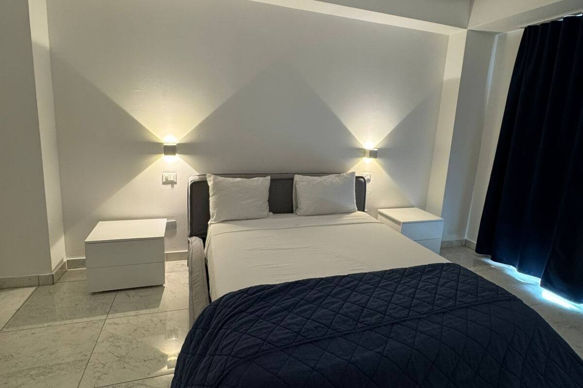 A modern bedroom with a large bed, bedside tables, and wall-mounted lighting.