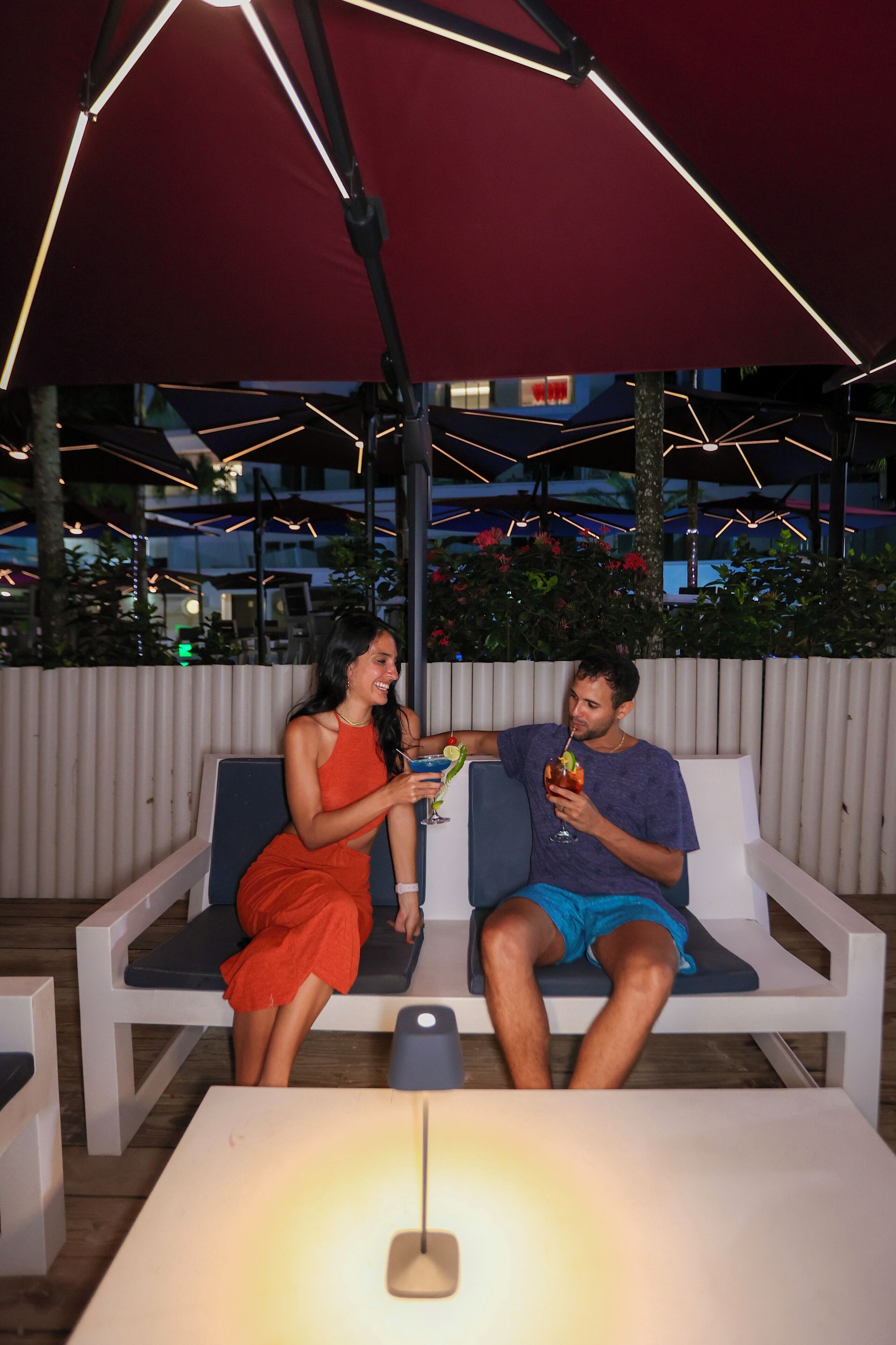 A couple seated on a white outdoor bench with a table in front.