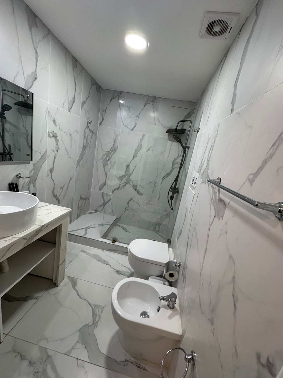 Ein modernes Badezimmer mit Marmorwänden, einer Dusche, einer Toilette, einem Bidet und einem Waschtisch.