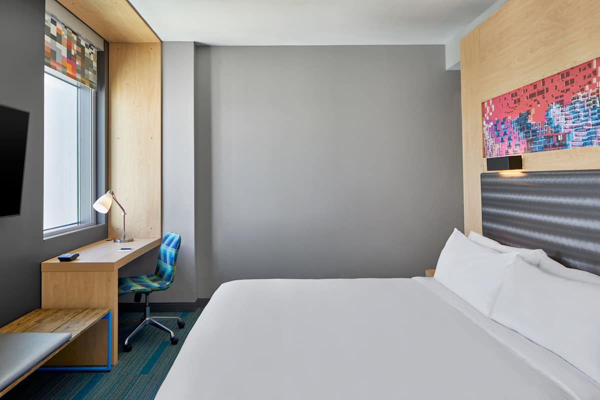 A hotel room with a bed, a desk with a chair, a TV, and a window.