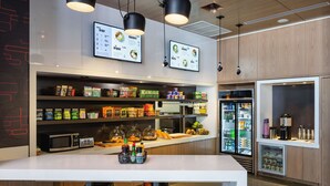 Un área de cocina moderna con encimera blanca, taburetes negros, microondas y un refrigerador lleno de bebidas.