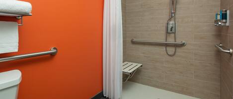 Ein Badezimmer mit orangefarbener Wand, Toilette in Weiß, Dusche inklusive Haltegriff und weißem Duschvorhang.