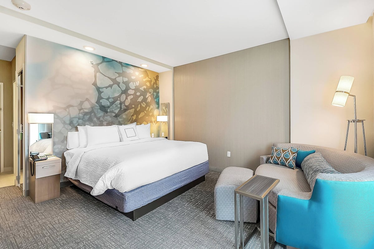 Ein modernes Hotelzimmer mit einem großen Bett, einer Couch, einem kleinen Tisch und einer Wand mit einem einzigartigen, abstrakten Design.