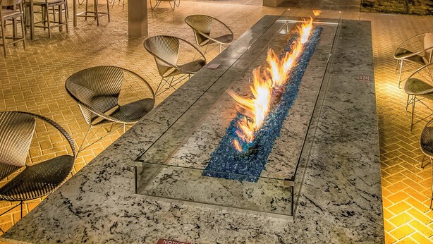 A fire feature with seating around it, a tiled floor, and a glass partition. - Courtyard by Marriott Longview North (Longview)