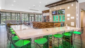 A modern bar area with a long counter, green cushioned bar stools, and a wooden accent wall. - Courtyard by Marriott Longview North (Longview)