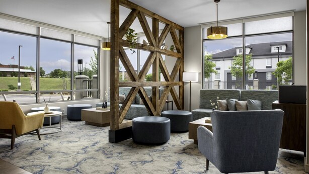 A modern lobby with large windows, a wooden accent wall, and a seating area with ottomans and a sofa. - Hilton Garden Inn Jackson (Jackson)