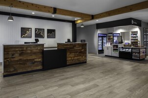 A hotel reception area with a wooden reception desk, a counter with a digital display, and a shop with various items.