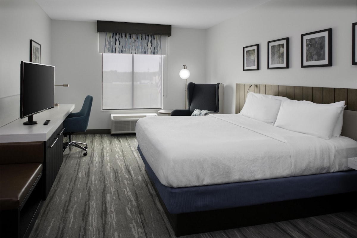 A hotel room with a bed, desk, chair, television, and a window with curtains.