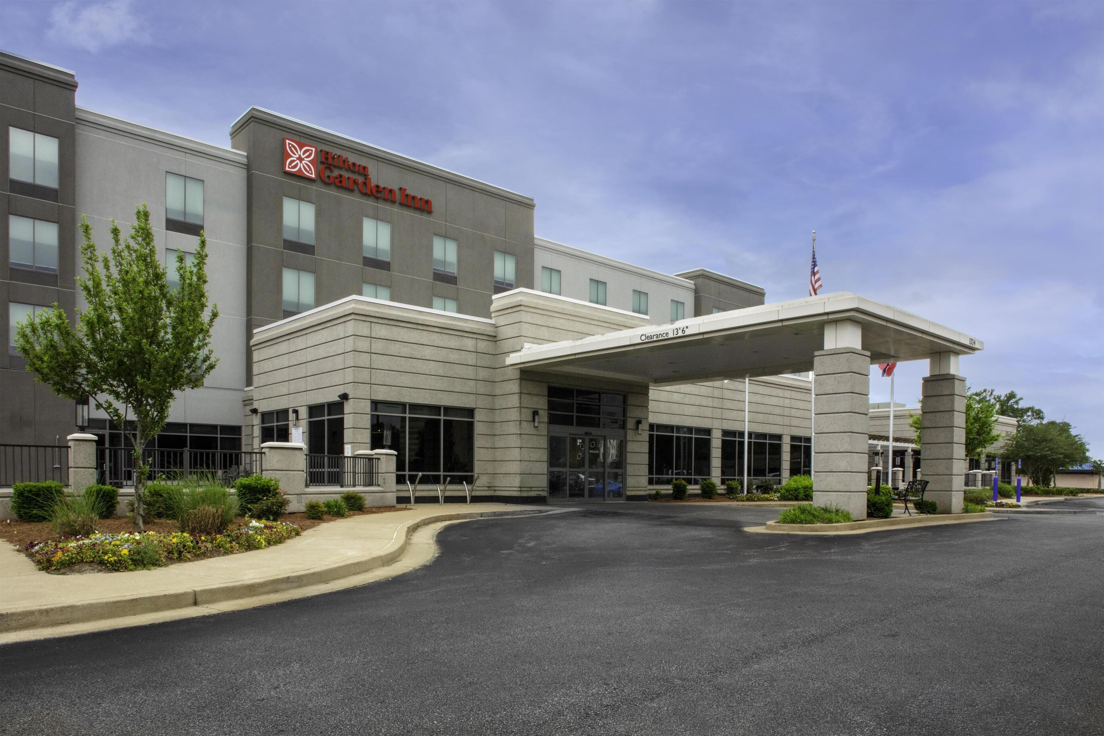 A hotel with a clear entrance, a sign reading 'Hilton Garden Inn,' and a flagpole with an American flag.