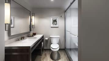 A modern bathroom with a large mirror, two sinks, a toilet, and a glass shower enclosure.