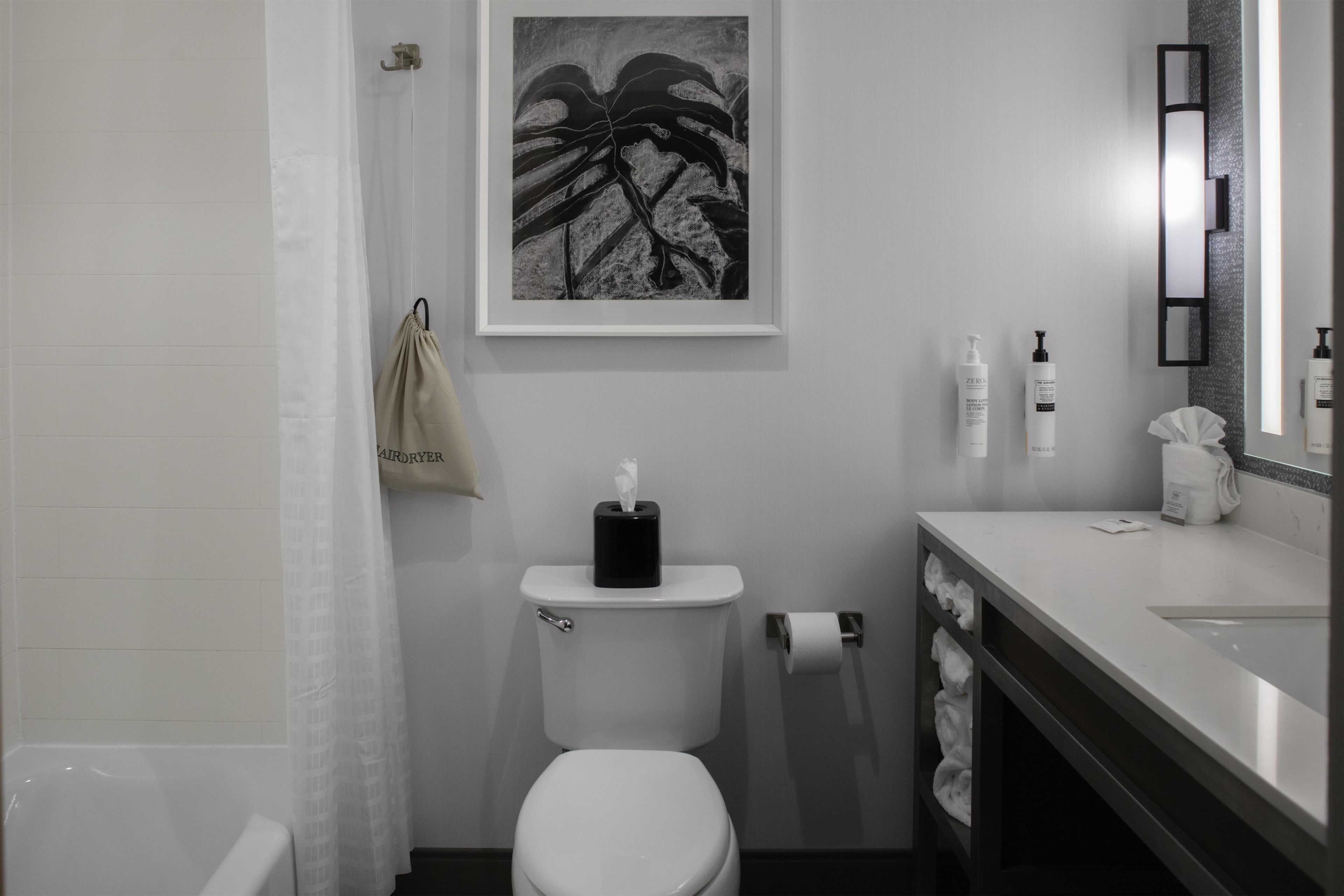 Ein modernes Badezimmer mit Toilette, Waschbecken, Handtuchhalter und einem gerahmten Kunstwerk an der Wand.