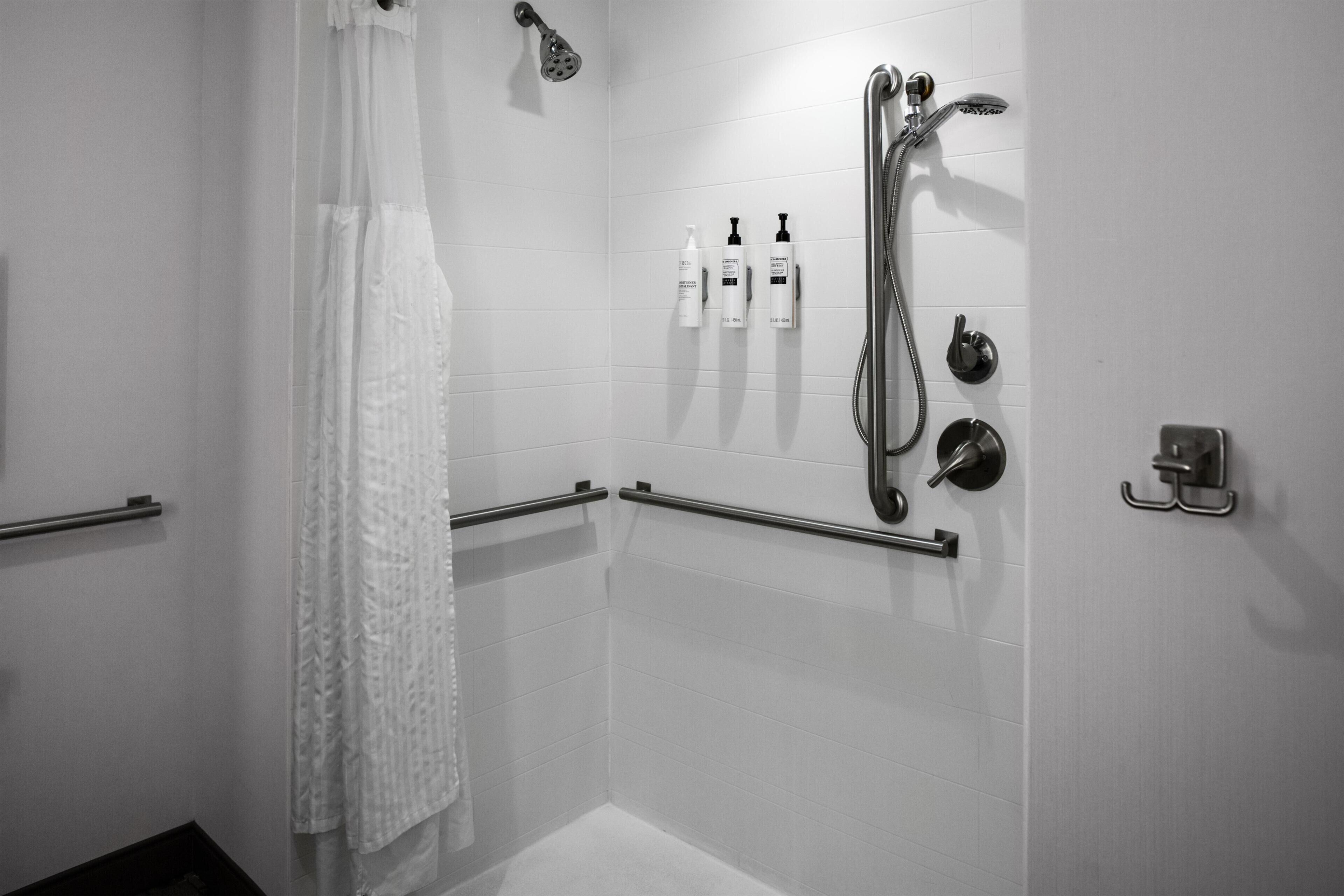 A shower area with a handheld showerhead, a wall-mounted faucet, and handrails.