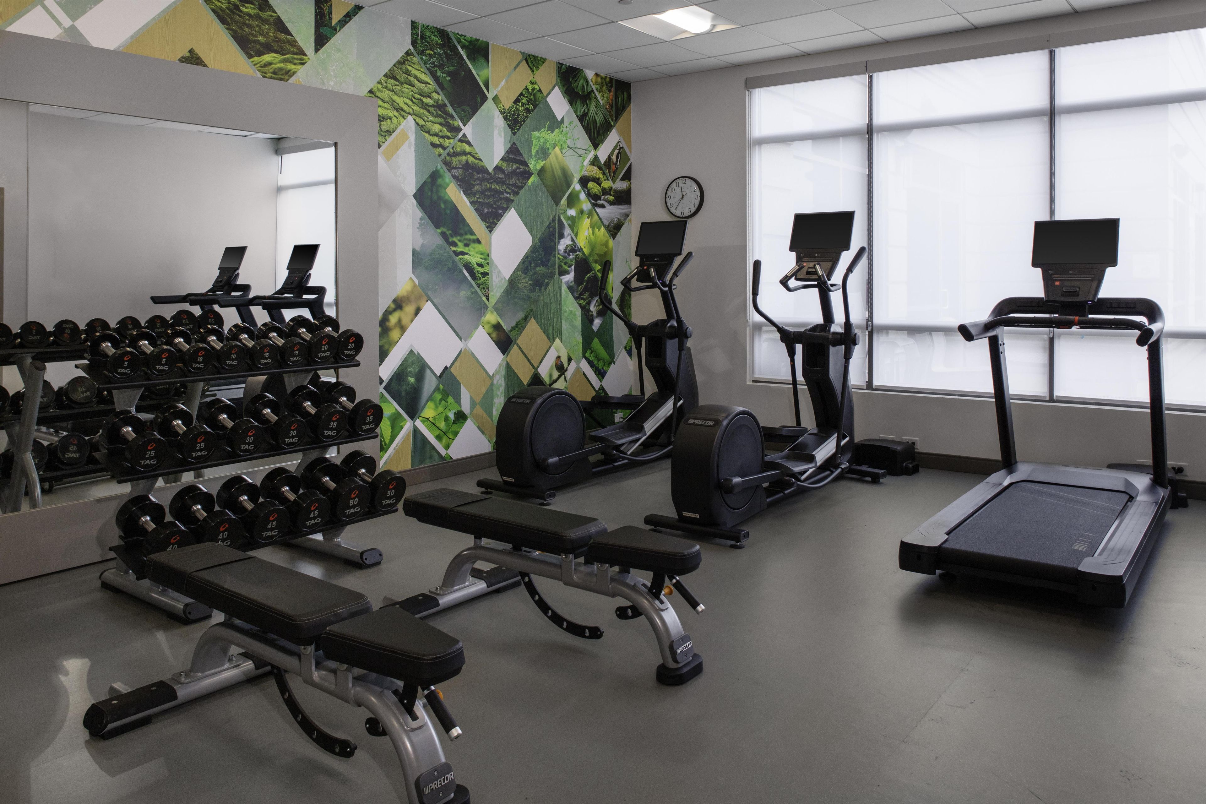 A gym with exercise equipment, a bench, dumbbells, and a wall with a geometric pattern.
