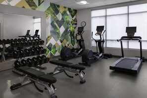 Un gimnasio con equipo de ejercicio, una banca, mancuernas y una pared con un diseño geométrico.