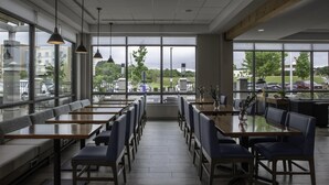 A spacious indoor seating area with tables and benches, large windows offering views of the parking lot and buildings outside. - Hilton Garden Inn Jackson (Jackson)
