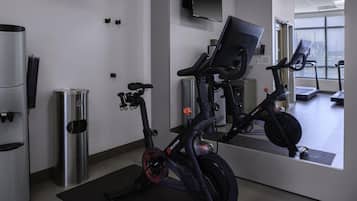 A gym with stationary bikes, a water dispenser, and a large mirror reflecting the room.