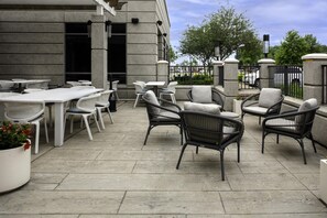 An outdoor patio area with tables and chairs, a potted plant, and a building with a stone facade. - Hilton Garden Inn Jackson (Jackson)