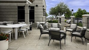 An outdoor patio area with tables and chairs, a potted plant, and a building with a stone facade. - Hilton Garden Inn Jackson (Jackson)