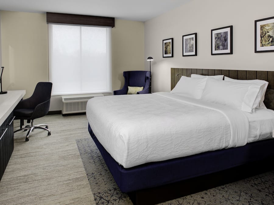 A hotel room with a large bed, a desk with a computer, a chair, and a window with blinds.