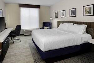 Habitación de hotel con una cama grande, un escritorio con computadora, una silla y una ventana con persianas.